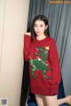 A woman wearing a red sweater with a green dinosaur on it.