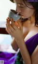 A woman in a purple dress drinking from a cup.