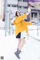 A woman in a yellow jacket is standing in the snow.