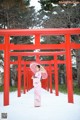 A woman in a pink kimono standing in front of a red torii gate.