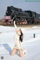 A woman in a white sweater and hat posing in front of a train.