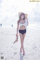 A woman in a bikini and hat walking on the beach.