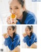 A woman eating a piece of fruit while wearing a blue sweatshirt.