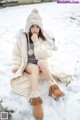 A woman sitting in the snow wearing a white coat and hat.