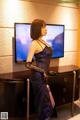 A woman in a purple dress standing in front of a television.