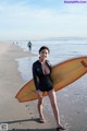 A woman in a wet suit holding a surfboard on the beach.