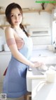 A woman in an apron standing in a kitchen next to a sink.