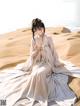 A woman in a white dress sitting on a sandy beach.