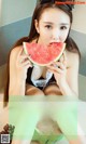 A woman eating a slice of watermelon in a bathtub.