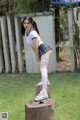 A young woman in a school uniform is posing on a tree stump.