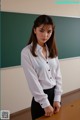 A woman in a white shirt and black skirt standing in front of a blackboard.