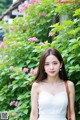 A woman in a white dress standing in front of pink flowers.